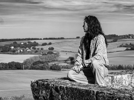 Femme méditant sur un rebord de mur, avec un paysage verdoyant en arrière-plan.