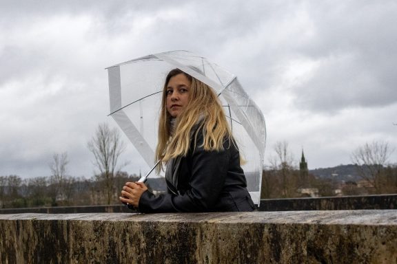 Femme avec un parapluie transparent sous un ciel nuageux, posant pensivement.